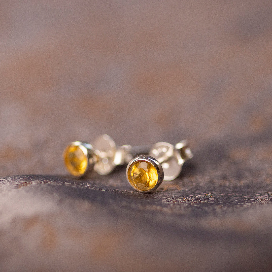 Citrine mini stud earrings in silver sitting on piece of fabric