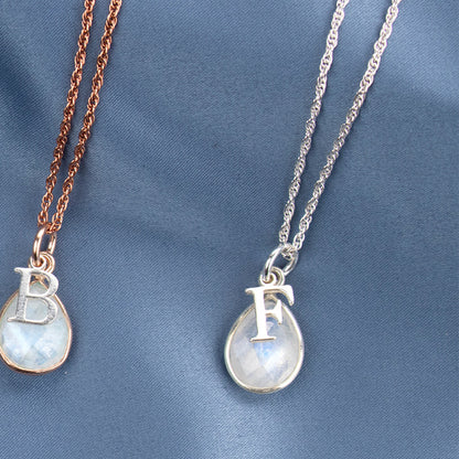 two moonstone charm necklaces with silver initial charms on a white background 