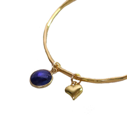 close up of sapphire charm bangle in gold with heart charm on a white background