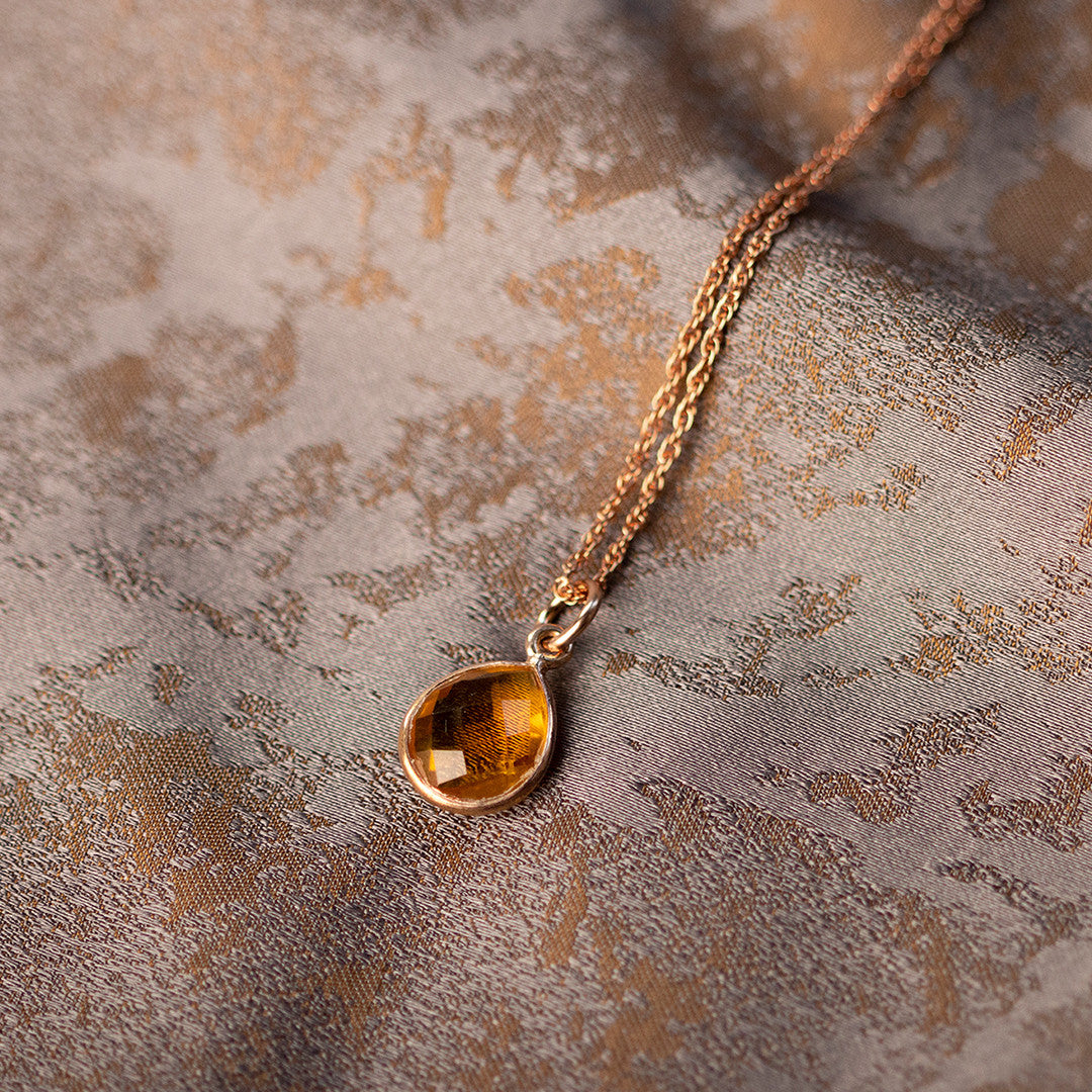 rose gold citrine charm necklace in rose gold on a piece of fabric