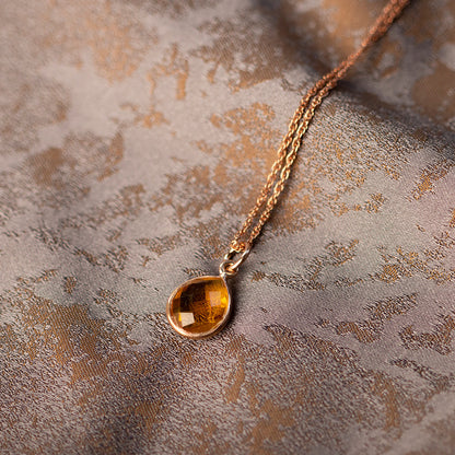 rose gold citrine charm necklace in rose gold on a piece of fabric