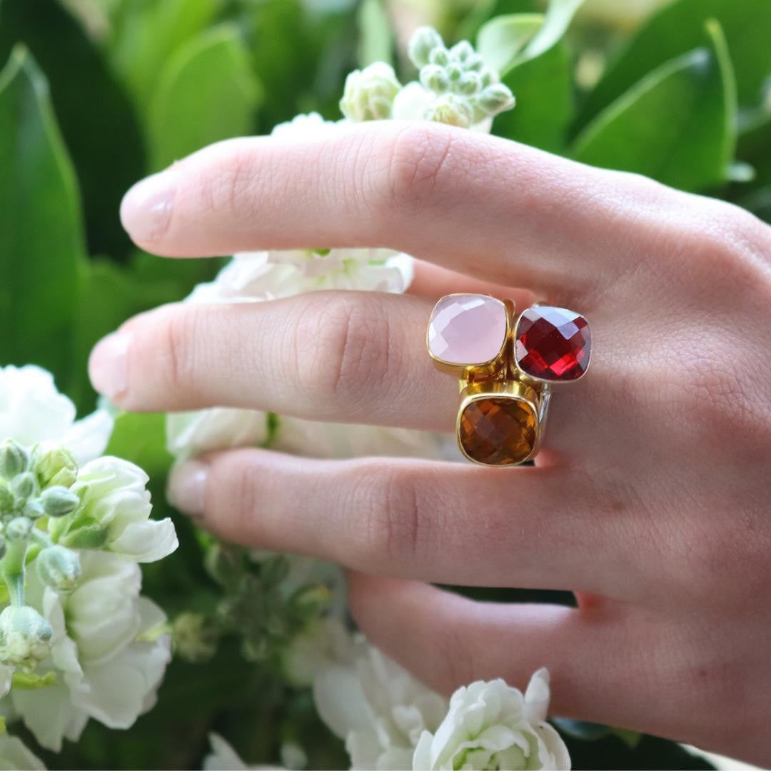 close up of model wearing stack of cocktail rings with flowers in the background