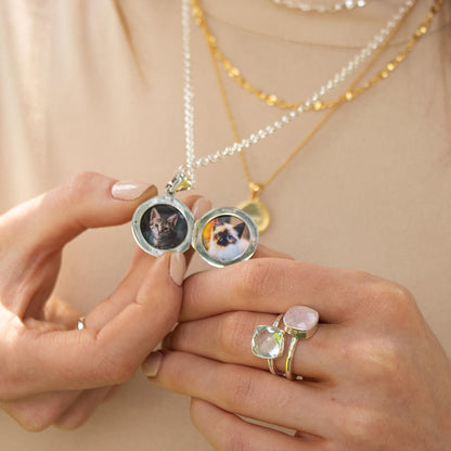 model holding feather locket whilst wearing two silver cocktail rings 