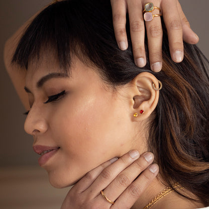 Model wearing garnet mini stud earrings in gold and showing rings