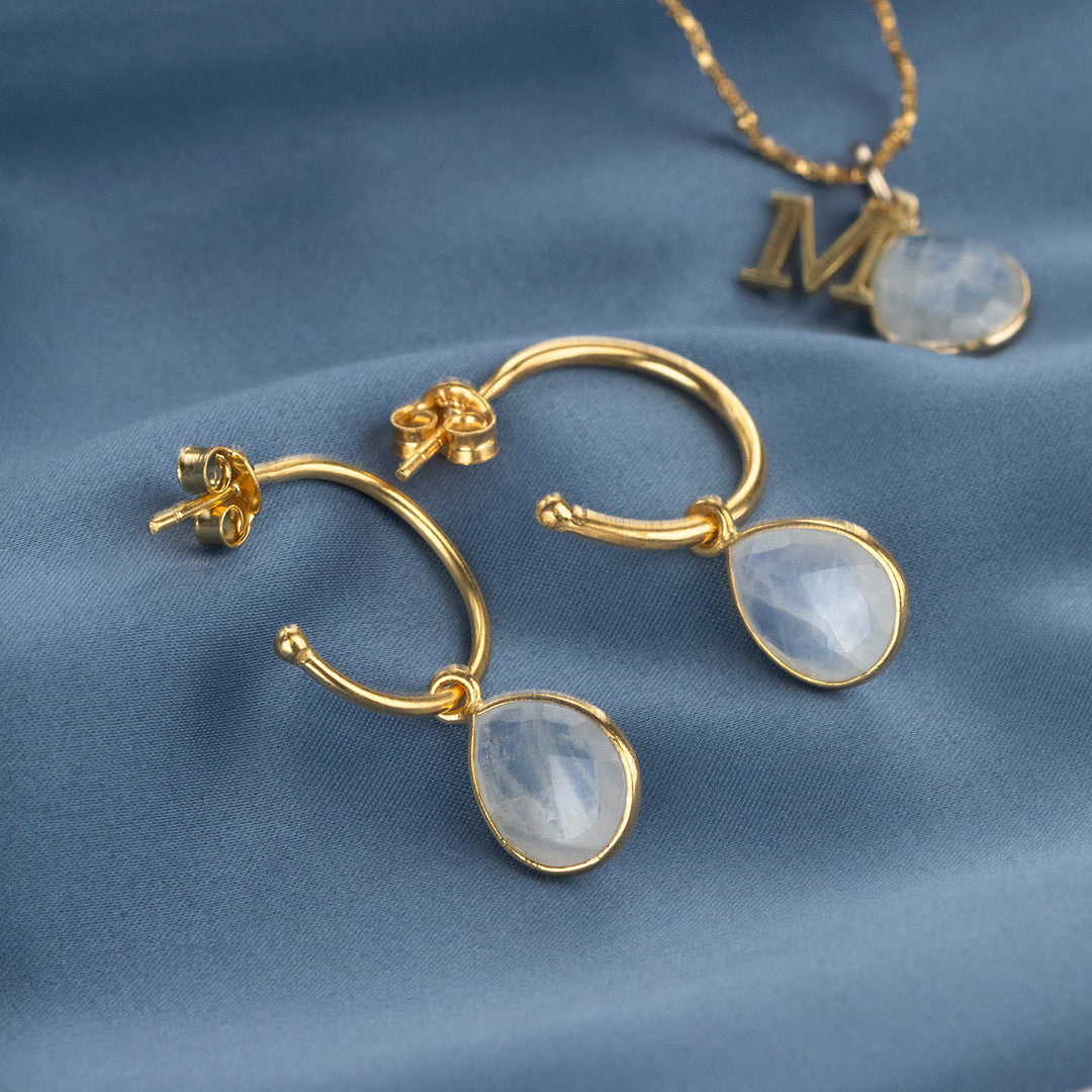drop hoop earrings in gold on a piece of blue fabric
