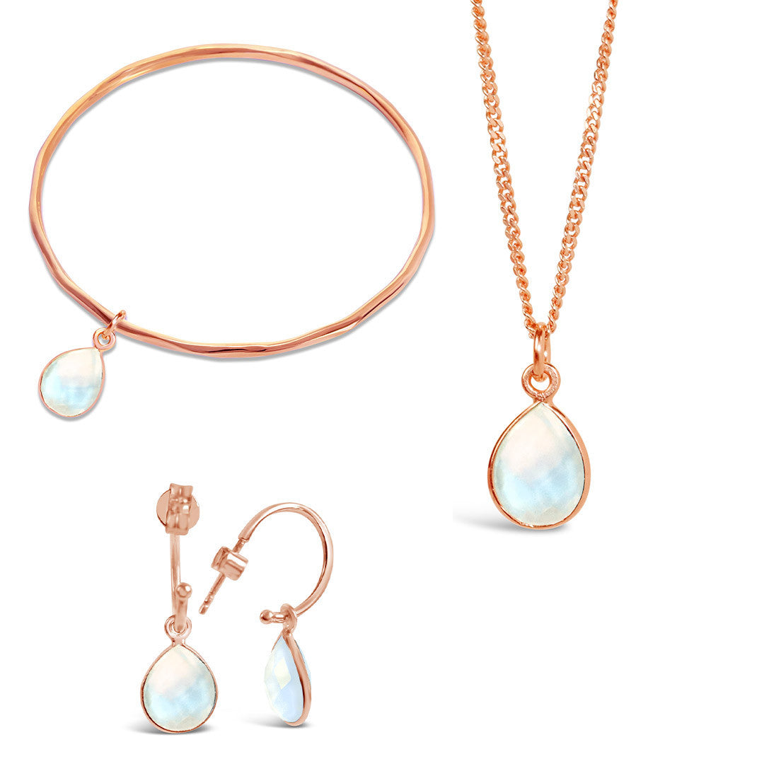 rose gold moonstone charm bangle, necklace and drop hoop earrings on a white background