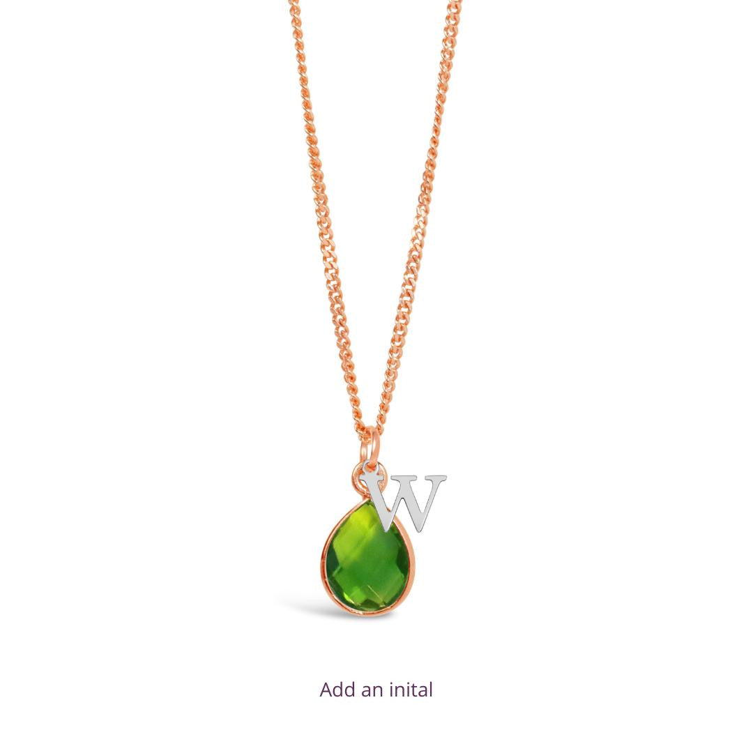 peridot charm necklace in rose gold with silver initial charm attached on a white background