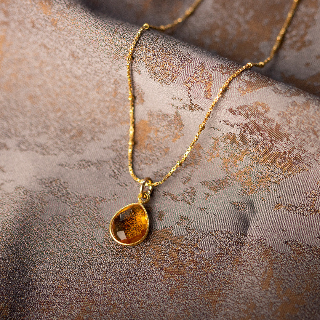 citrine charm necklace in gold on a piece of fabric