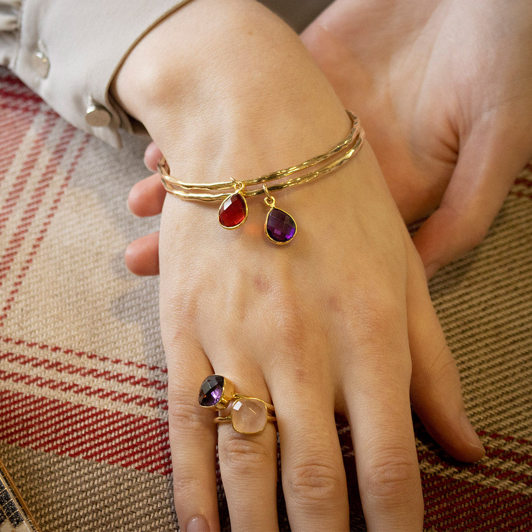 close up of models hands wearing two gold charm bangles with birthstones