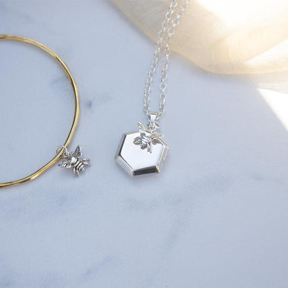 bee locket in silver with silver bee charm next to gold bangle
