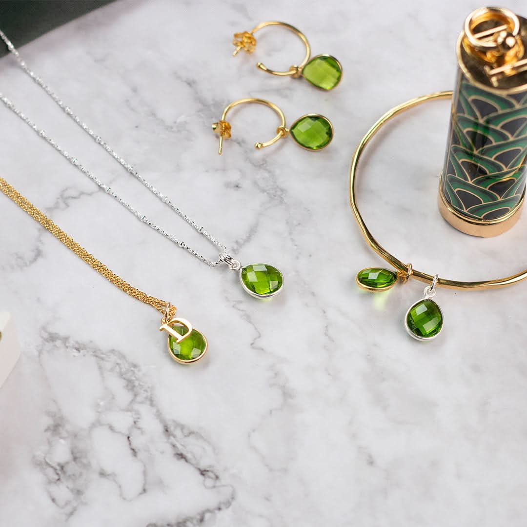 real green peridot teardrop gemstone on a gold thin bangle on a marble tile with other peridot jewellery