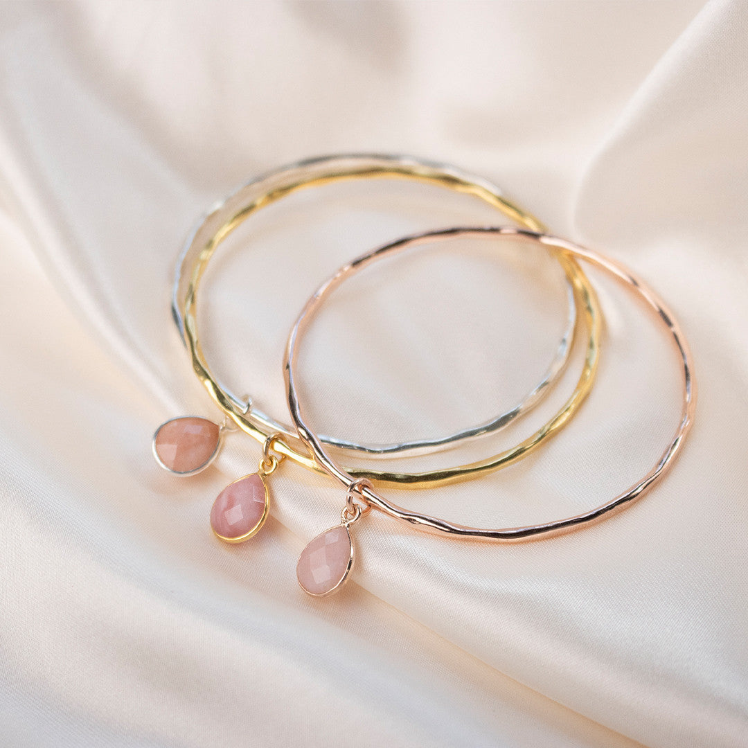 three pink opal charm bangles in gold on a white piece of fabric