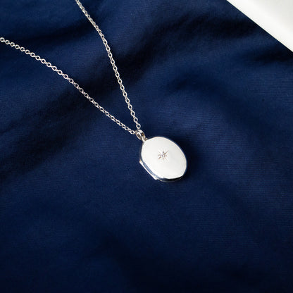 small oval diamond locket in silver on a piece of blue fabric