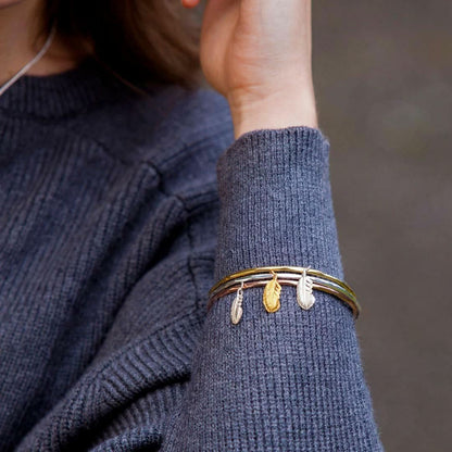 close up of model wearing three feather bangles on her wrist