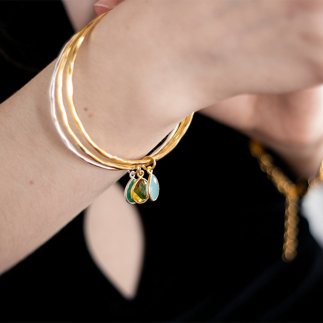close up of models arm wearing three charm bangles with birthstones
