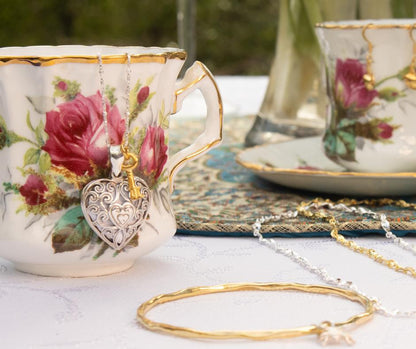 white gold heart locket hanging out of tea cup with flowers on it