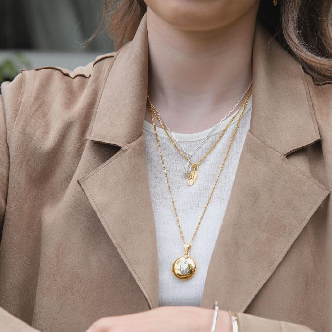 model wearing gold feather locket with silver feather charm