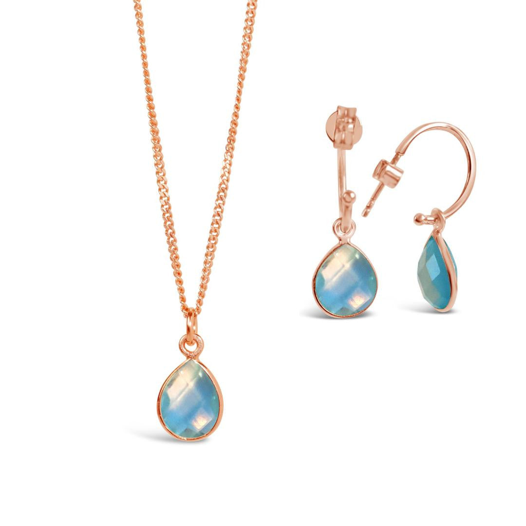 blue topaz charm necklace and drop hoop earrings in rose gold on a white background