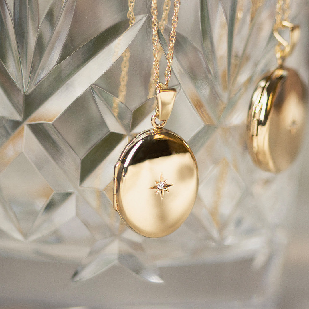 two oval diamond lockets in gold hanging out of glass