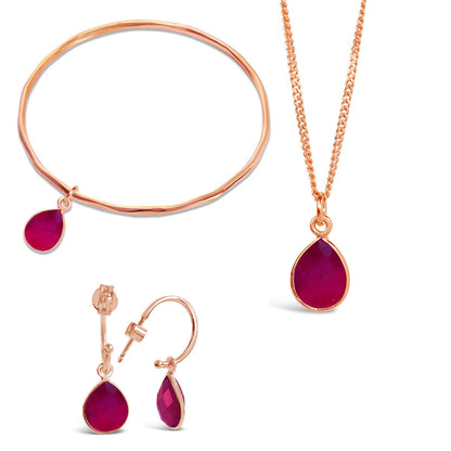 rose gold ruby charm bangle, necklace and drop hoop earrings on a white background