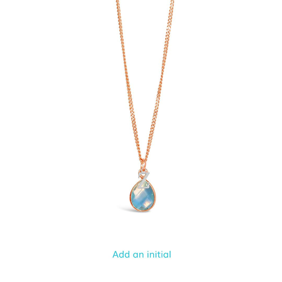 blue topaz charm necklace with silver initial charm in rose gold on a white background