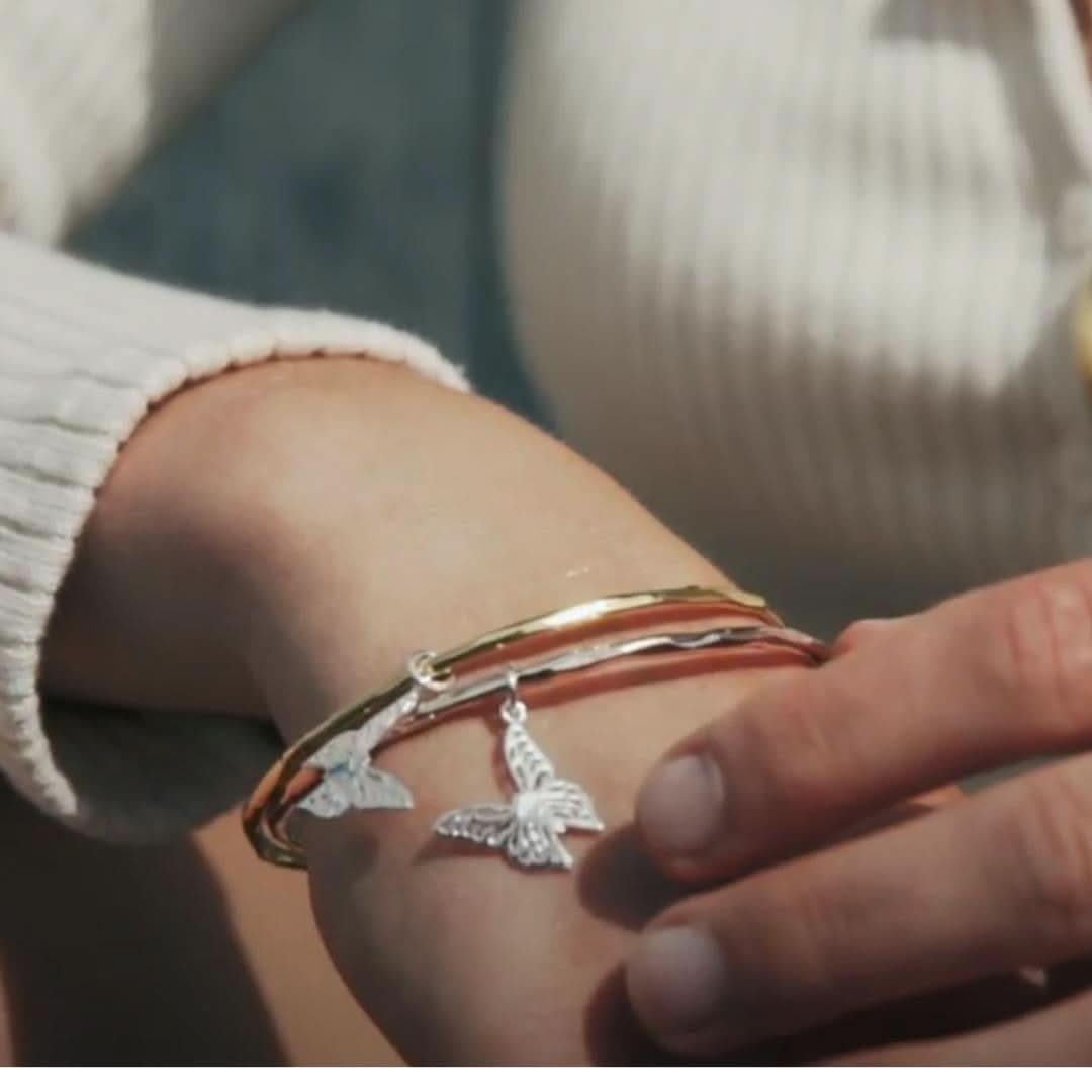 close up of model wearing rose gold bangle with silver butterfly charm attached 