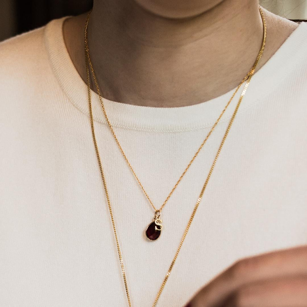 model wearing garnet charm necklace in gold with initial charm
