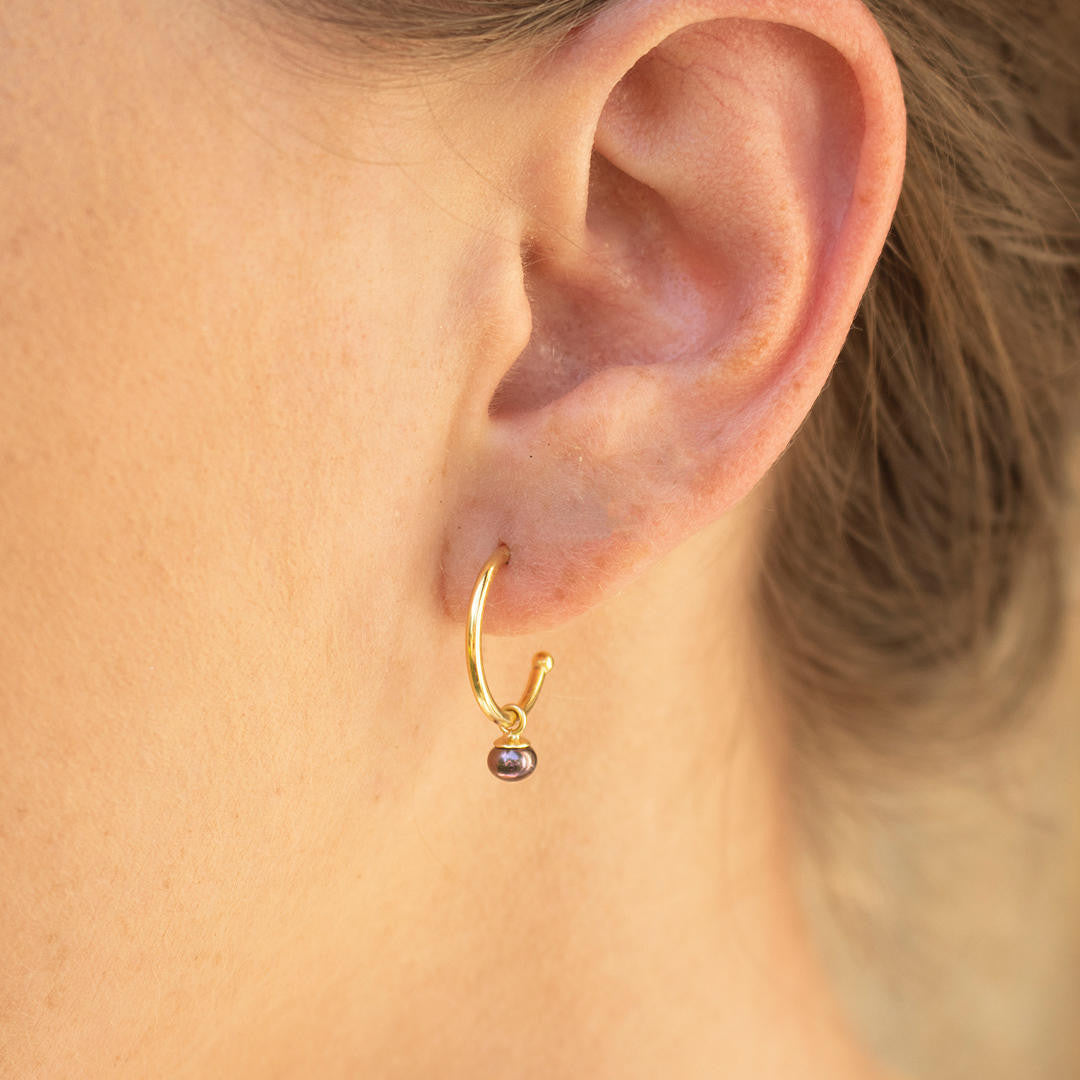close up of model wearing dainty pearl drop hoop earrings in midnight gold