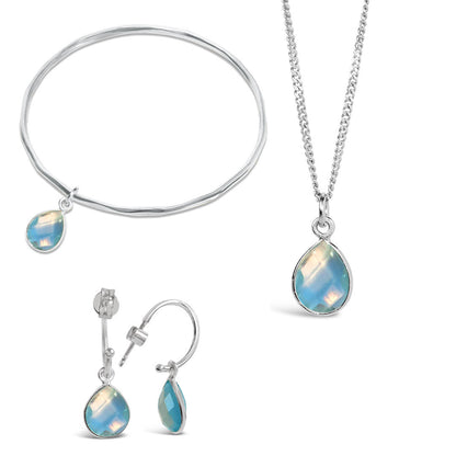 blue topaz silver charm bangle, necklace and drop hoop earrings on a white background
