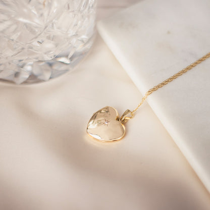 diamond heart locket in gold next to a glass