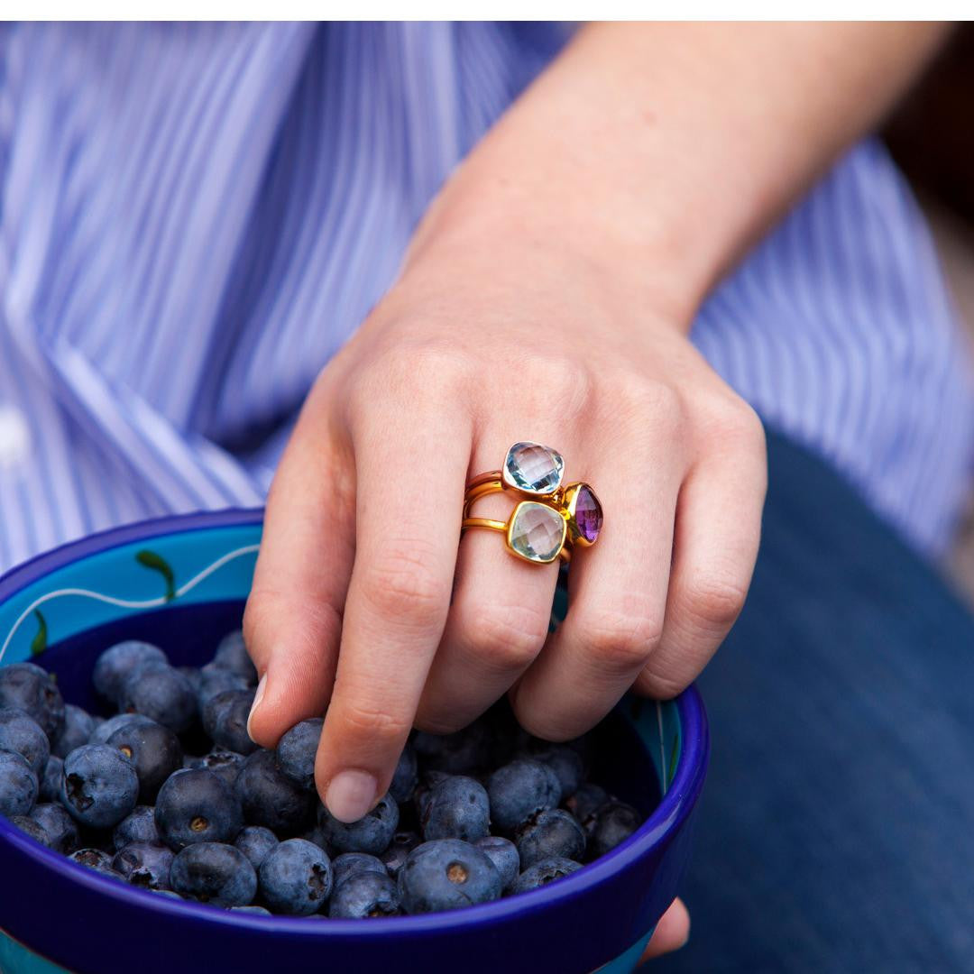 model wearing blue topaz cocktail ring in gold with bowl of blueberries