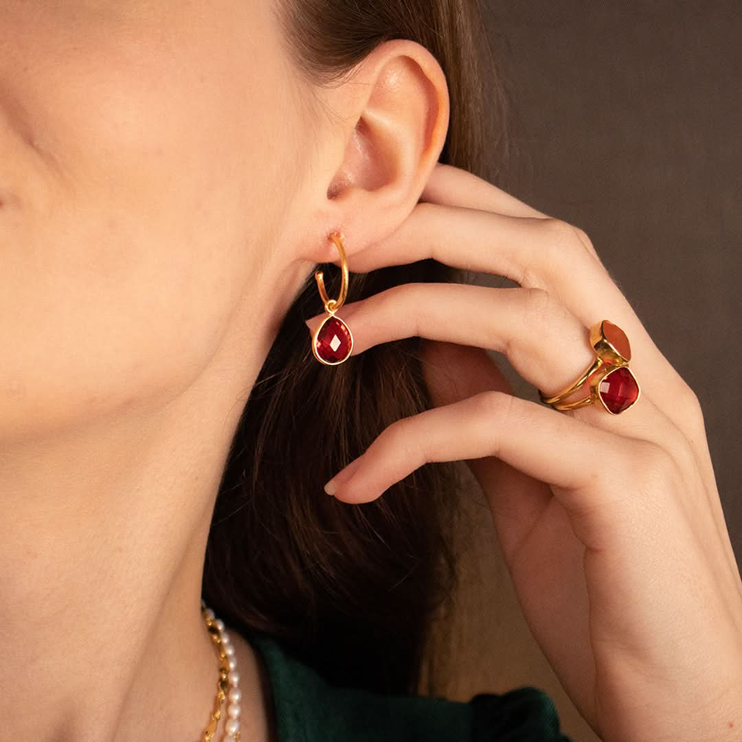 closeup of model wearing garnet drop hoop earrings in gold