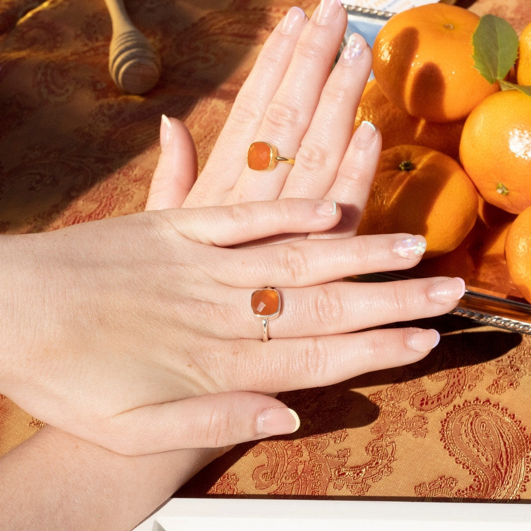 model wearing two carnelian cocktail rings  next to basket of oranges