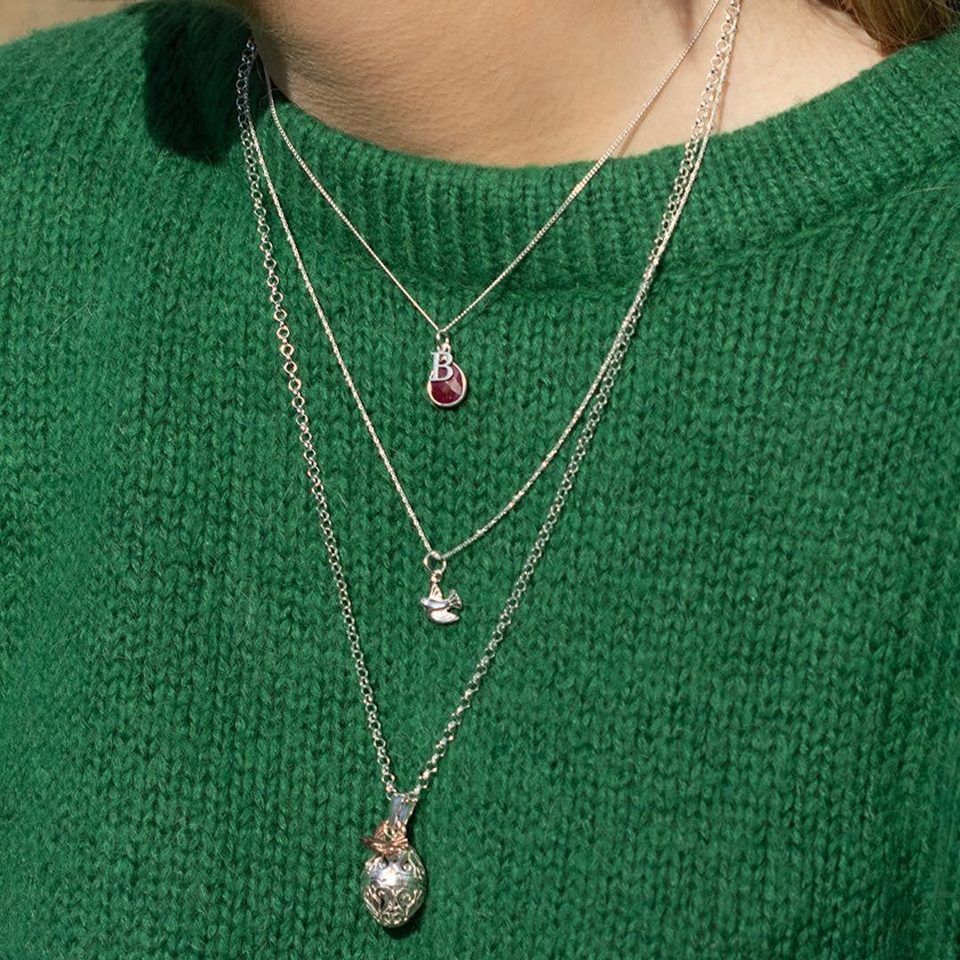 model in jumper wearing silver necklace with ruby gemstone charm