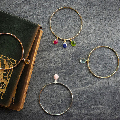four gold charm bangles with birthstones and a book on a piece of grey fabric