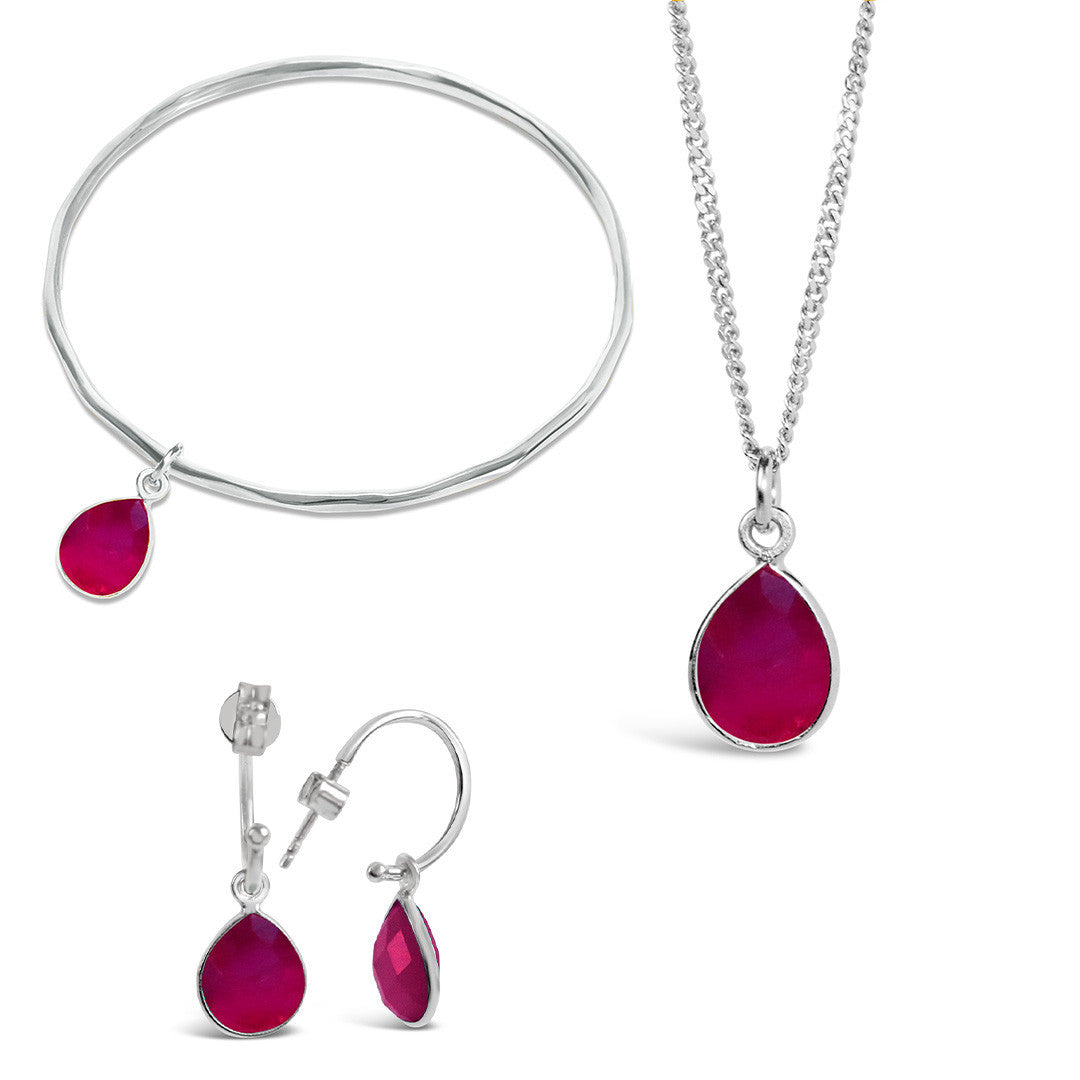 silver ruby charm bangle, necklace and drop hoop earrings on a white background