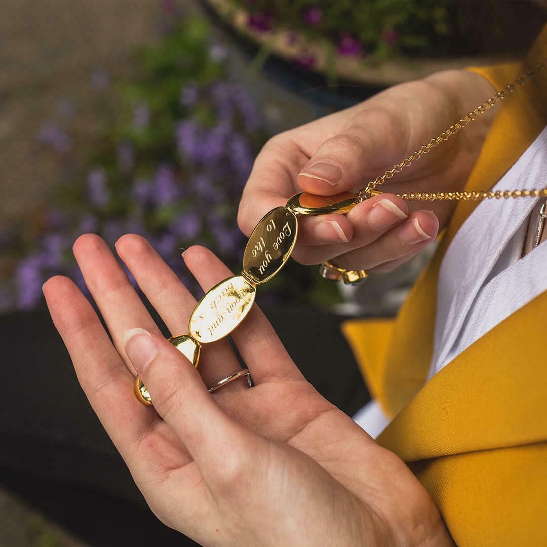model holding gold oval shaped locket with engraved message