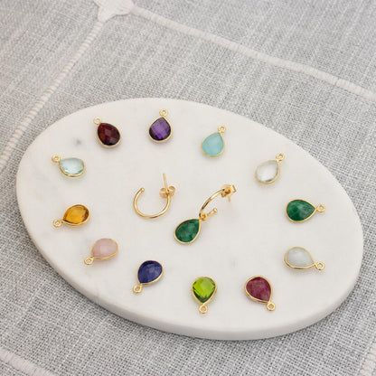 gold birthstones and drop hoop earrings in gold on a white platter