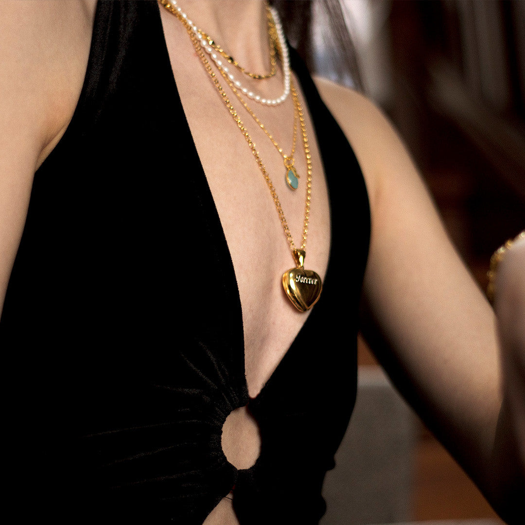 model in black dress wearing gold heart shaped locket with engraved message