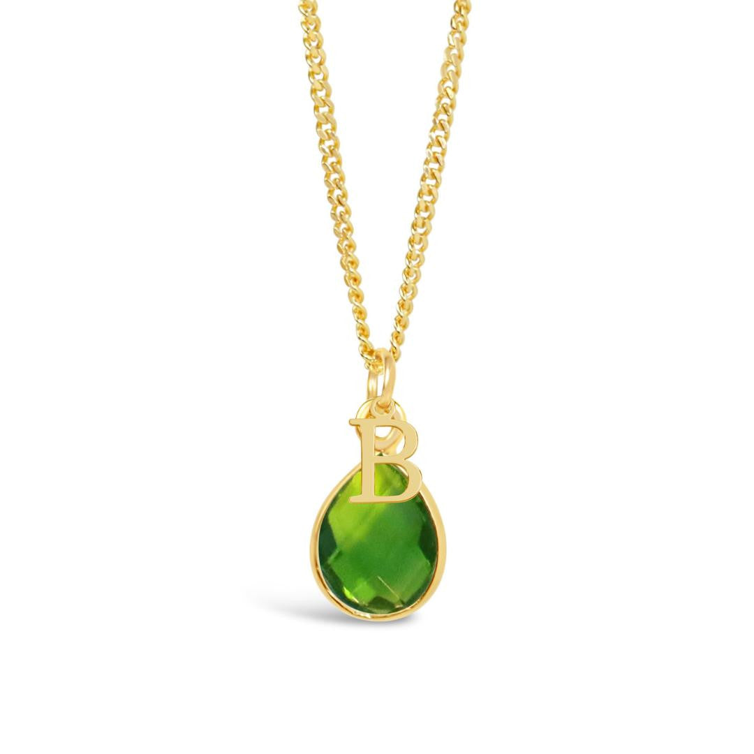 peridot charm necklace in gold with initial charm attached on a white background