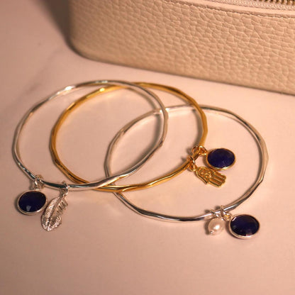 three sapphire charm bangles with different charms attached 