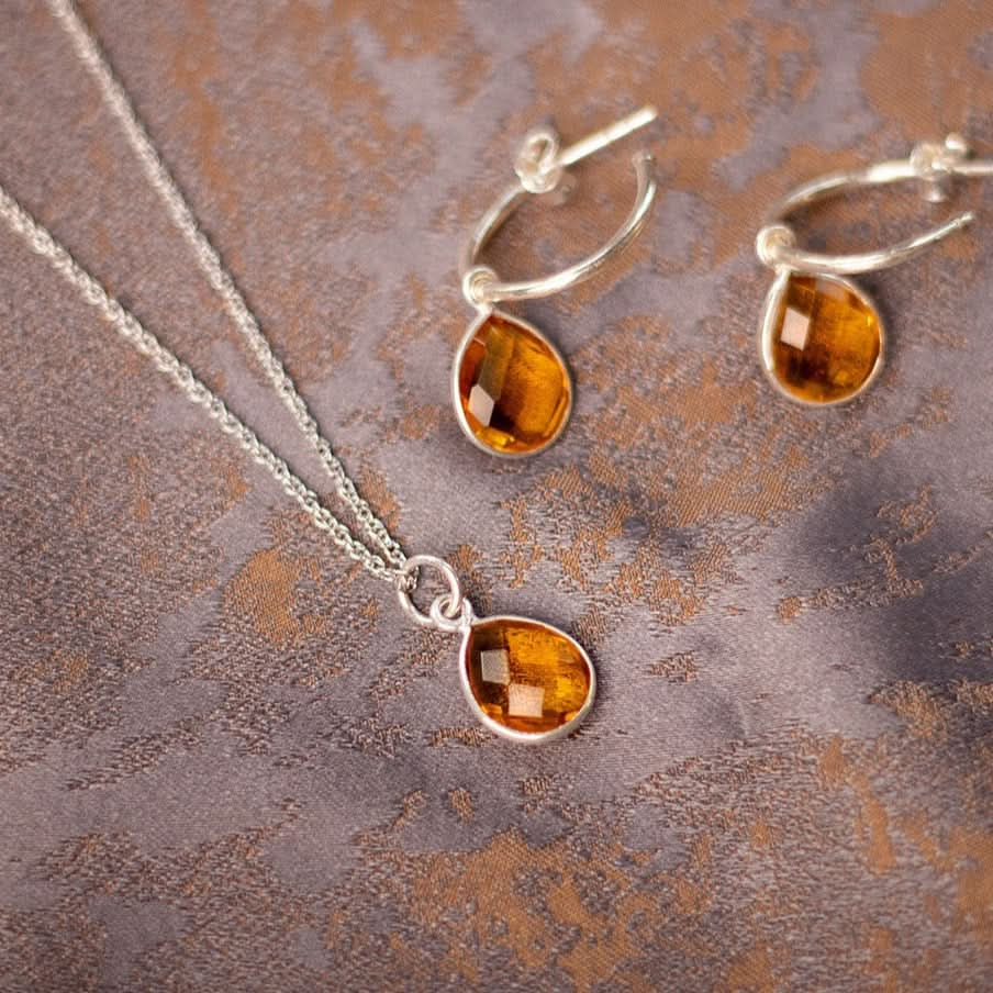 citrine charm necklace and drop hoop earrings in silver on a piece of fabric