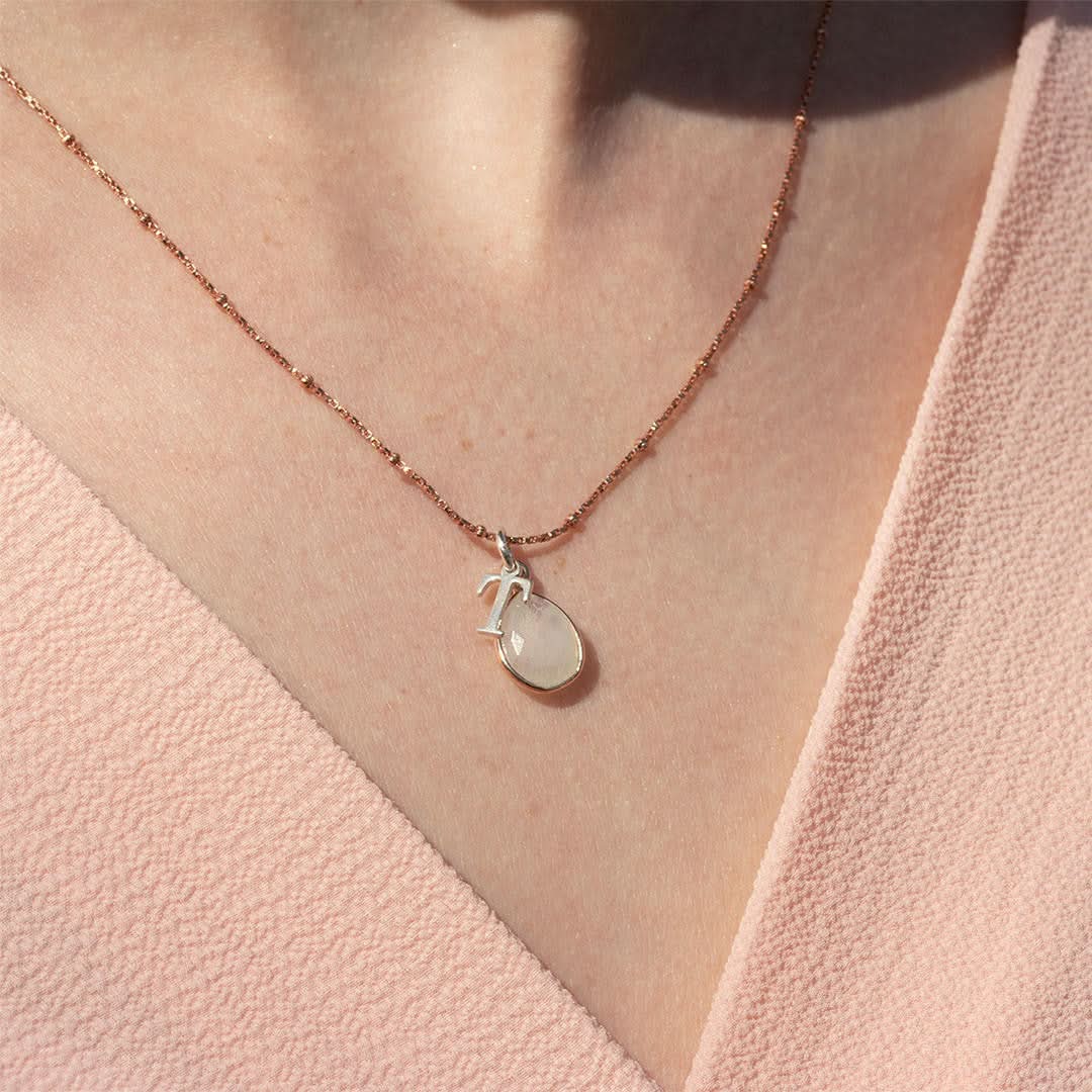 close up of model in a pale pink top wearing moonstone charm necklace in rose gold with silver initial T charm