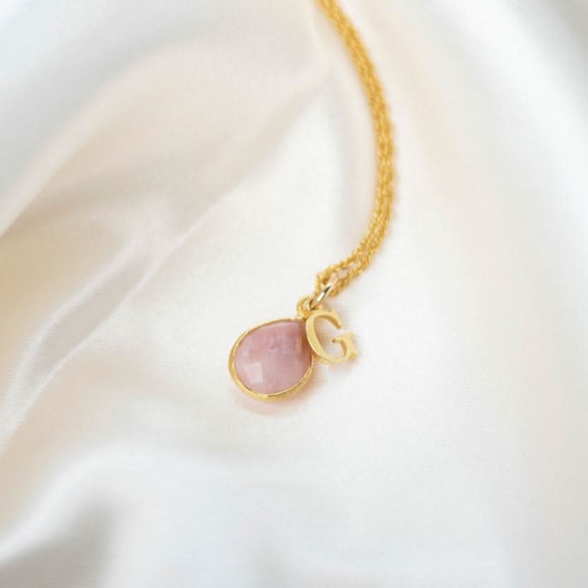 pink opal charm necklace in gold with initial charm on a piece of fabric