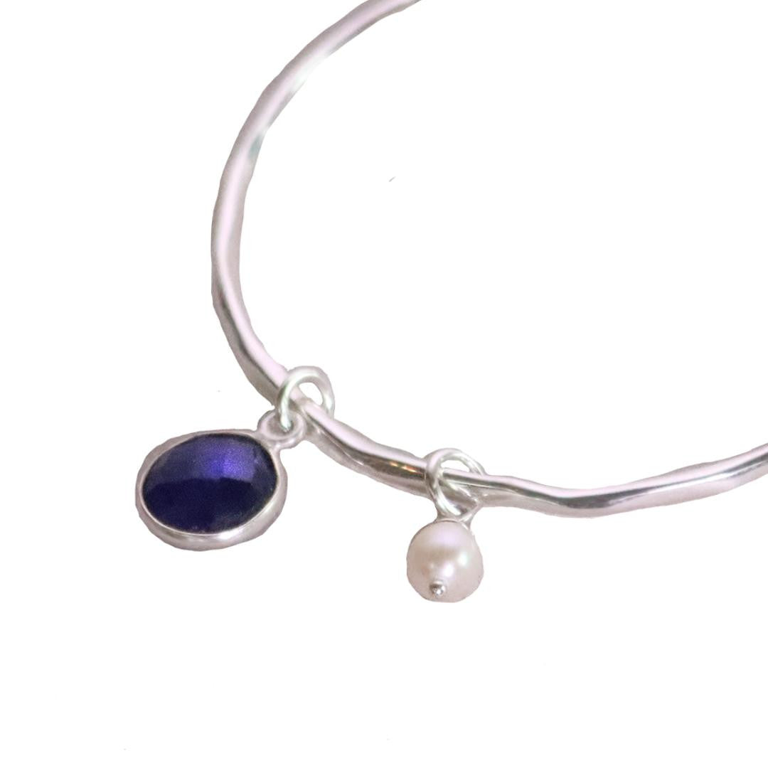 close up of sapphire charm bangle with silver pearl attached 