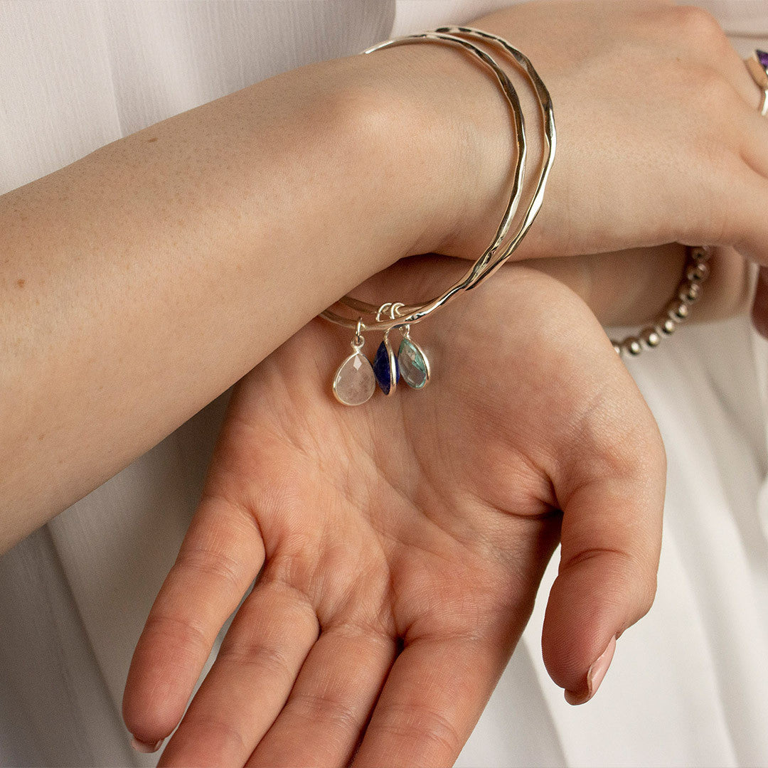 model wearing two silver bangles with birthstones attached 