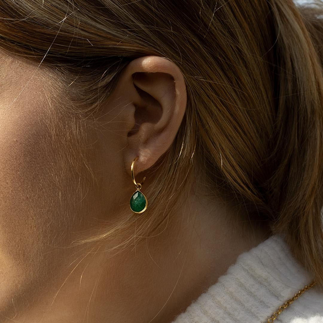closeup of model wearing emerald drop hoop earrings in gold