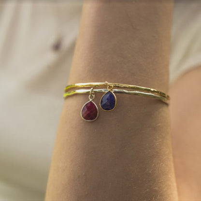 close up of models arm wearing two gold charm bangles with birthstones