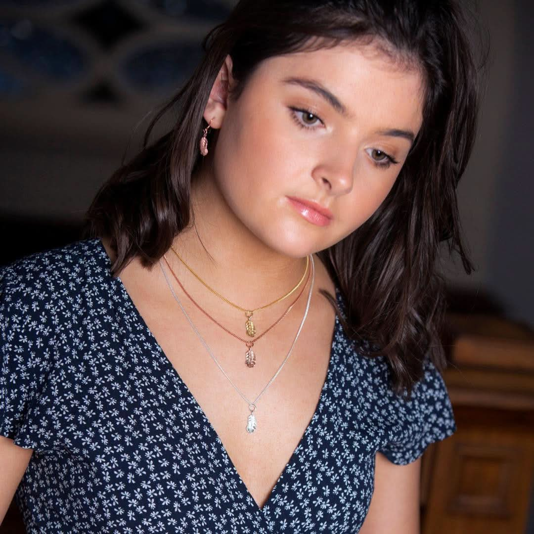 model wearing three feather pendants in rose gold, silver and gold