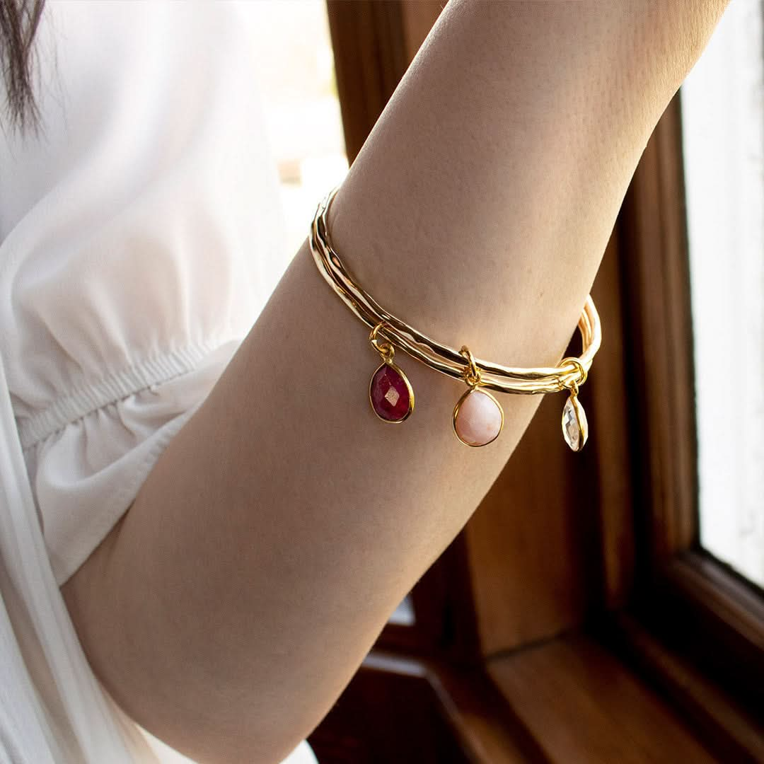 close up of model wearing two gold charm bangles with birthstones